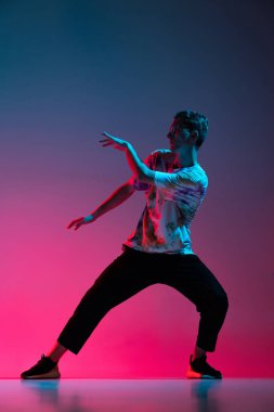 Hip-hop dansı yapan genç adamın dikey portresi neon ışıklarıyla izole edilmiş pembe arkaplanda izole edilmiş.