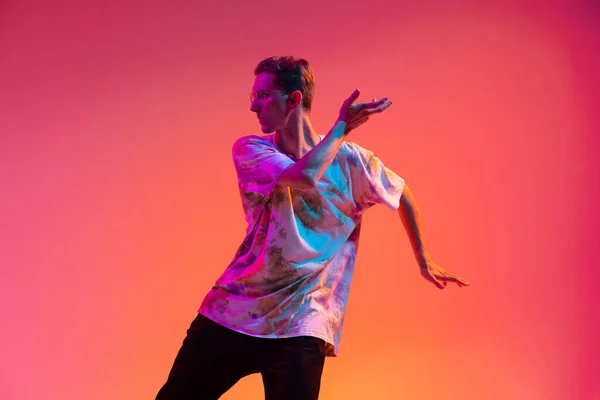 ネオンの光の中でグラデーションの黄色のピンクのスタジオの背景に隔離されたヒップホップダンスを練習魅力的な若い男のトリミングされた肖像画 — ストック写真