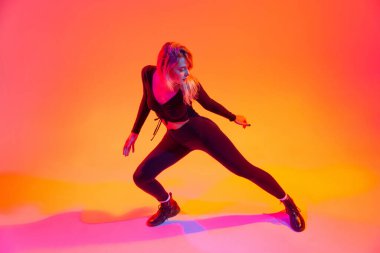 Genç, güzel, beyaz bir kız dans ediyor. Renkli turuncu arka planda, neon ışıkta izole edilmiş. Sokak dansı