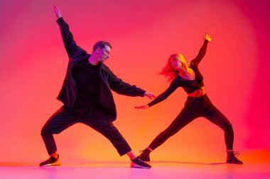 Hareket halindeki iki genç erkek ve kadın hip-hop dansçısının portresi neon ışıklarıyla izole edilmiş.