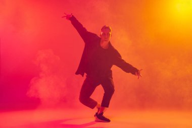 Şık siyah elbiseli, hip-hop dansı yapan beyaz bir çocuk. Duman içinde parlak pembe arka planda izole edilmiş.