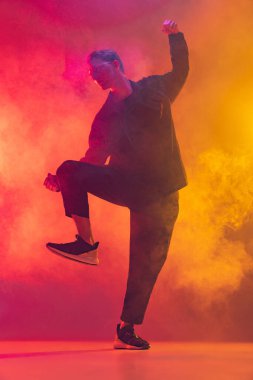 Şık siyah elbiseli, hip-hop dansı yapan beyaz bir adam. Duman içinde parlak pembe arka plan üzerinde izole edilmiş.