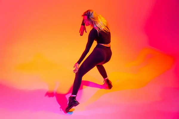 Giovane bella ragazza caucasica danza isolato su sfondo arancione sfumato in luce al neon. Hip-hop in movimento — Foto Stock