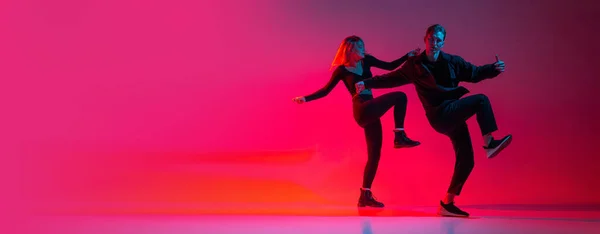 ネオンの光の中でピンクのグラデーションスタジオの背景に孤立したダイナミックな若者と女性がヒップホップを踊る。フライヤー — ストック写真
