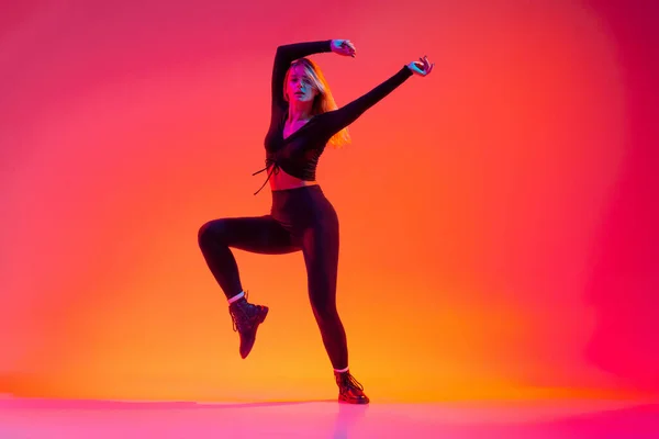 Actieve flexibele jonge blanke vrouw dansen hip-hop geïsoleerd over gradiënt roze gele achtergrond in neon licht — Stockfoto