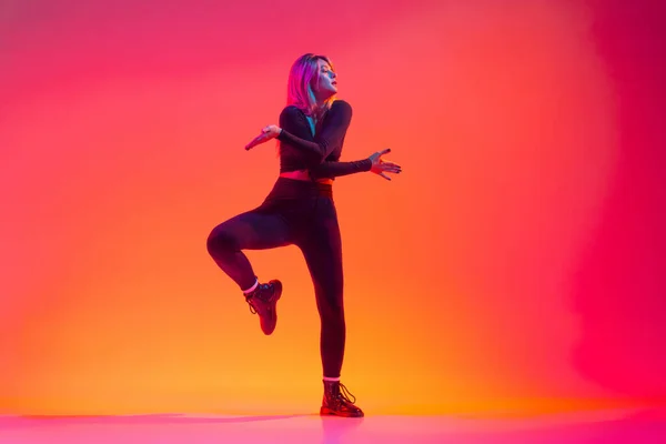 Full-length portret van mooie sportieve blanke meisje dansen hip-hop geïsoleerd over verloop roze gele achtergrond in neon licht — Stockfoto