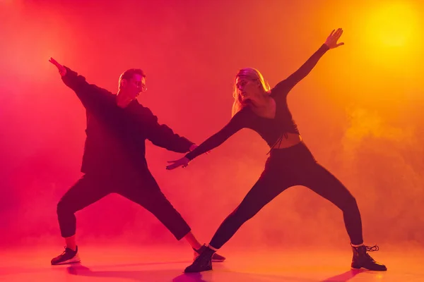 Retrato de dois jovens dançarinos de hip-hop masculinos e femininos em movimento isolados sobre gradiente de fundo amarelo rosa em luz de néon em fumaça — Fotografia de Stock