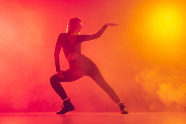 Mulher branca nova em roupas pretas elegantes dançando hip-hop isolado sobre gradiente rosa fundo amarelo em luz de néon na fumaça — Fotografia de Stock