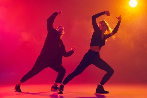 Vista inferior de dois jovens dançarinos de hip-hop em movimento isolados sobre gradiente de fundo amarelo-rosa em luz de néon em fumaça — Fotografia de Stock