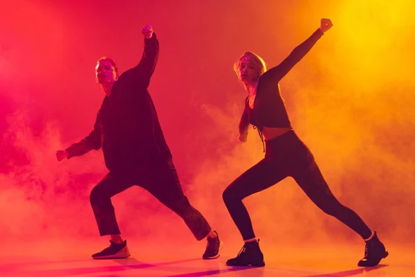 Dois jovens dançarinos de hip-hop em movimento isolados sobre gradiente rosa fundo amarelo em luz de néon em fumaça — Fotografia de Stock