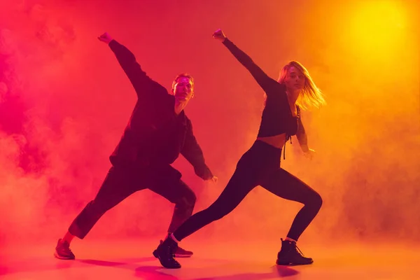 Vista inferior de dois jovens dançarinos de hip-hop em movimento isolados sobre gradiente de fundo amarelo-rosa em luz de néon em fumaça — Fotografia de Stock