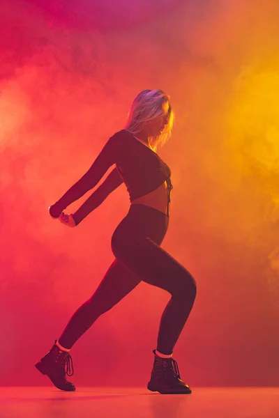 Potrait of Caucasian girl dancing hip-hop isolated over gradient pink yellow background in neon light in smoke — ストック写真