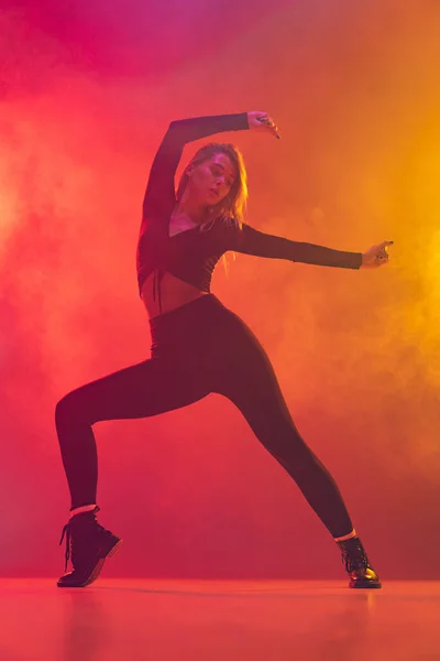 Vista lateral da menina caucasiana dançando hip-hop isolado sobre gradiente rosa fundo amarelo em luz de néon na fumaça — Fotografia de Stock