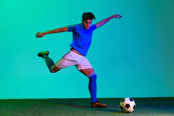 Pełnowymiarowy portret młodego profesjonalnego piłkarza odizolowanego na niebieskim tle. W ruchu. — Zdjęcie stockowe