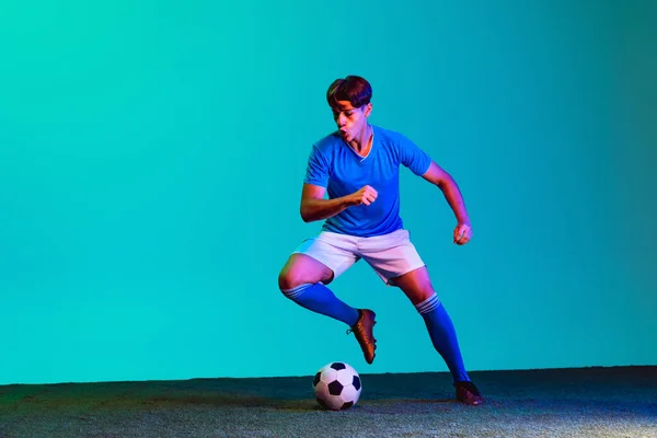 Retrato completo de un joven futbolista caucásico entrenando activamente aislado sobre fondo azul — Foto de Stock