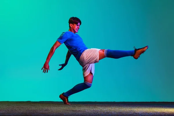 Retrato de un joven futbolista caucásico entrenando activamente aislado sobre fondo azul — Foto de Stock