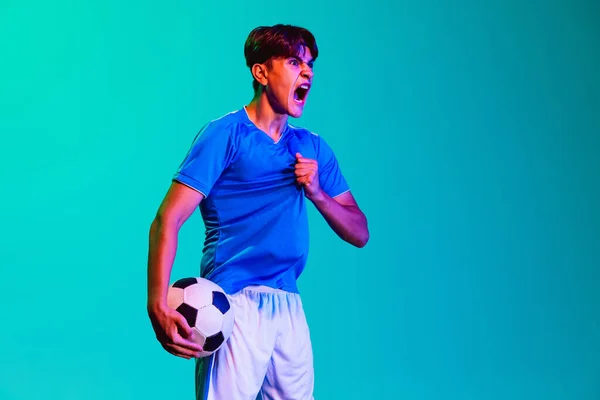 Młody zawodowy piłkarz odizolowany na niebieskim tle. Zwycięstwo gry — Zdjęcie stockowe