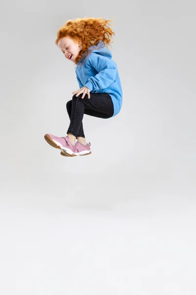 Porträtt av liten vit flicka, barn hoppar och poserar isolerad över grå studio bakgrund. — Stockfoto