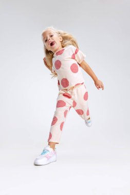 Küçük beyaz bir kızın tam boy portresi, beyaz stüdyo arka planında izole bir şekilde koşan bir çocuk..