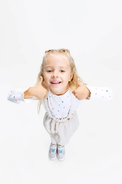 Bovenaanzicht portret van kleine blanke meisje, kind poseren geïsoleerd over witte studio achtergrond. Duimen omhoog. Heerlijk. — Stockfoto