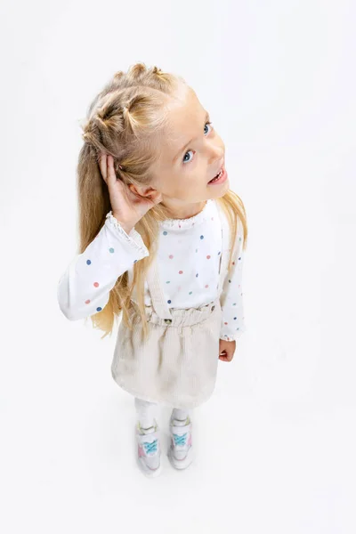 Retrato de pouco bonito menina pré-escolar posando com sua mão para orelha isolado sobre branco estúdio fundo. — Fotografia de Stock