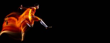 Genç sporcunun tam boy yatay portresi, futbol oyuncusu eğitimi siyah arka planda karışık ışıkta izole edilmiş. El ilanı