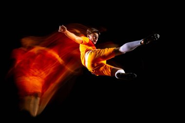 Genç sporcunun tam boy yatay portresi, futbol oyuncusu eğitimi siyah arka planda karışık ışık altında izole edilmiş.