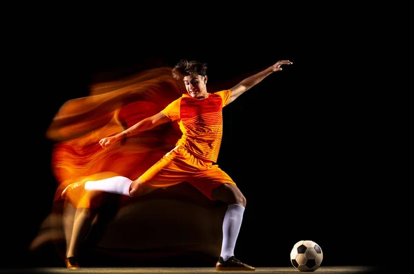 Młody profesjonalny piłkarz trening izolowany na czarnym tle w mieszanych światłach — Zdjęcie stockowe