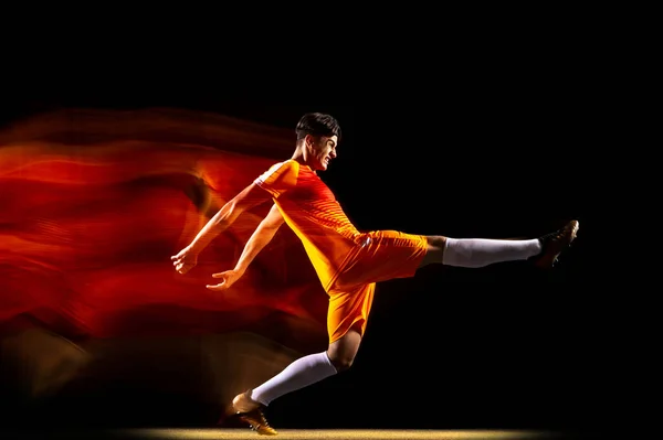 Retrato de jovem desportista, jogador de futebol treinando isolado sobre fundo preto em luz mista. Objetivo vencedor — Fotografia de Stock