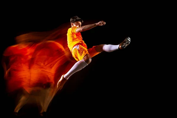 Potret horizontal lengkap dari olahragawan muda, pemain sepak bola yang bergerak terisolasi di atas latar belakang hitam dalam cahaya campuran — Stok Foto