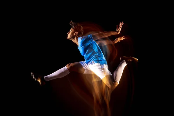 Jovem desportista, futebolista treinando isolado sobre fundo preto em luz mista. Em um salto — Fotografia de Stock