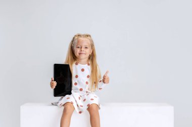 Beyaz stüdyo arka planında izole edilmiş tabletli küçük anaokulu kızının portresi..