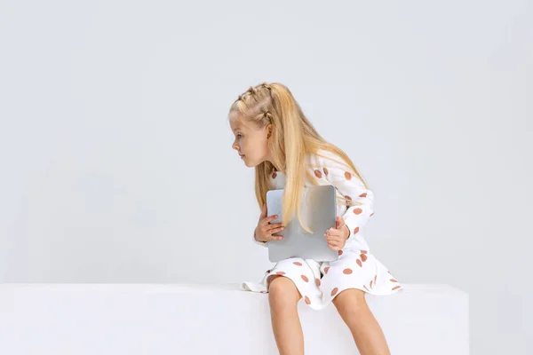 Retrato de pequena menina pré-escolar com tablet olhando para longe isolado sobre fundo estúdio branco. — Fotografia de Stock