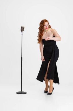 Beyaz arka planda izole edilmiş mikrofonlu güzel kadın şarkıcının tam boy portresi.