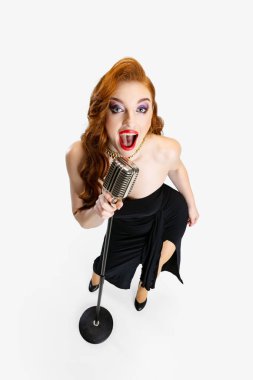 Beyaz arka planda izole bir şekilde mikrofonla şarkı söyleyen güzel kızıl saçlı kadının tam boy portresi.