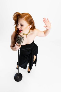 Beyaz arka planda izole bir şekilde mikrofonla şarkı söyleyen güzel kızıl saçlı kadının tam boy portresi.