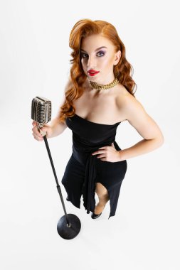 Beyaz arka planda izole bir şekilde mikrofonla şarkı söyleyen güzel kızıl saçlı kadının tam boy portresi.