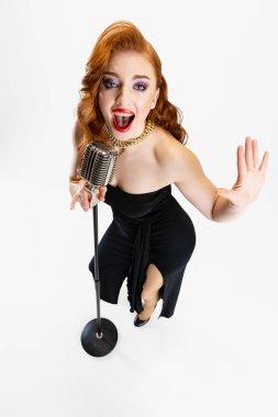Beyaz arka planda izole bir şekilde mikrofonla şarkı söyleyen güzel kızıl saçlı kadının tam boy portresi.
