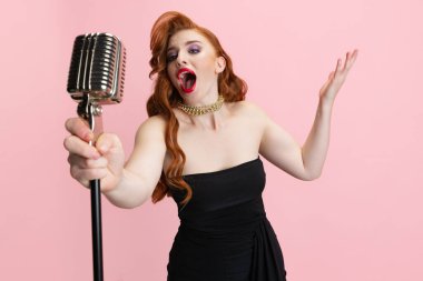 Pembe arka planda izole edilmiş mikrofonla şarkı söyleyen etkileyici güzel bir kadının stüdyo portresi. Retro müzik sanatçısı