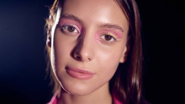 Close-up of woman with shimmering pink eye makeup and confident expression. Concept of radiance, empowerment, and fashion beauty for editorial and branding visuals.
