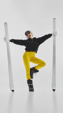 Joyful woman in yellow leggings posing playfully with skis in winter fashion style. Concept of confidence, energy, and youthful charm for influencer branding, athleisure fashion, and lifestyle visuals