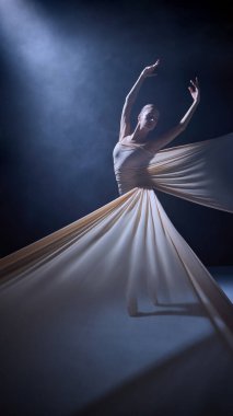 Sahne ışıkları altında kollarını açarak kumaşa sarılmış bir balerin. Sahne performansı, vücut uzantısı, ışıklandırma kompozisyonu ve dans eğitimi hassasiyeti kavramı.