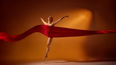 Kırmızı kumaşlı balerin turuncu sahne ışıkları altında sevinçle sıçrıyor. Editör, yaratıcı ve ticari tasarım için dans özgürlüğü, enerji ve sanatsal hareket kavramı.
