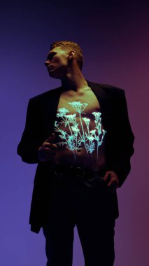 Göğsünde neon ışık yansıması olan siyah takım elbiseli bir adam menekşe arka planına karşı. Dijital kimlik, vücut aydınlatması ve tasarım ve reklamcılık için geleceksel ifade kavramı.