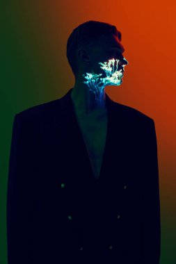 Siyah ceketli, yüzünde ve boynunda parlak botanik projeksiyonu olan bir adam. Kişisel farkındalık kavramı, doğayla bağlantı, yaratıcı reklamlar, moda ve sanat projeleri için kişisel büyüme