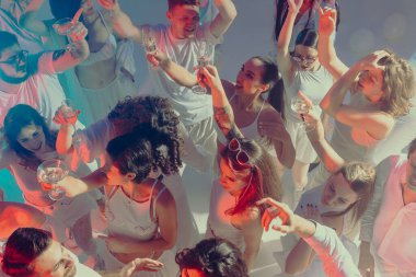 Neşeli beyaz partisinde pembe ışıklarla kutlama yapmak için gülümseyen insanlar. Etkinlik ve eğlence temaları için modern sosyal yaşam tarzı, arkadaşlık enerjisi ve editoryal görseller kavramı.