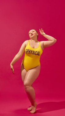 Pembe arka planda zarifçe poz veren sarı mayolu büyük beden bir model. Kendine güvenen zarafet, canlı vücut pozitifliği, kampanyalar, güzellik markaları ve dergiler için moda güçlendirme kavramı..