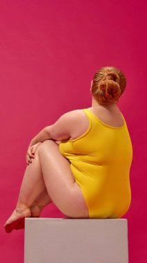 Sarı mayo giymiş, büyük beden bir kadının arka görüntüsü en düşük kompozisyonda. Sakin kuvvet kavramı, vücut kabulü, dergiler, kampanyalar ve sağlık projeleri için moda zarafeti.