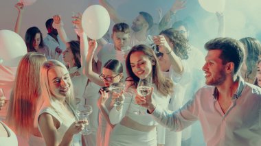 Bir grup genç kadeh kaldırıyor ve beyaz temalı kutlama partisinde gülümsüyor. Arkadaşlık kavramı, birlik, mutluluk ve yaşam tarzı modern neşe ile birlikte..