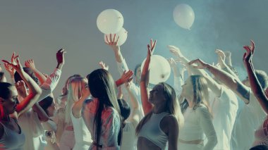 Sahne ışıklarının altında balonlarla beyaz dans eden heyecanlı kalabalık. Eğlence enerjisi kavramı, gençlik kültürü ve duygu ve hareketle dolu dijital sosyal atmosfer.
